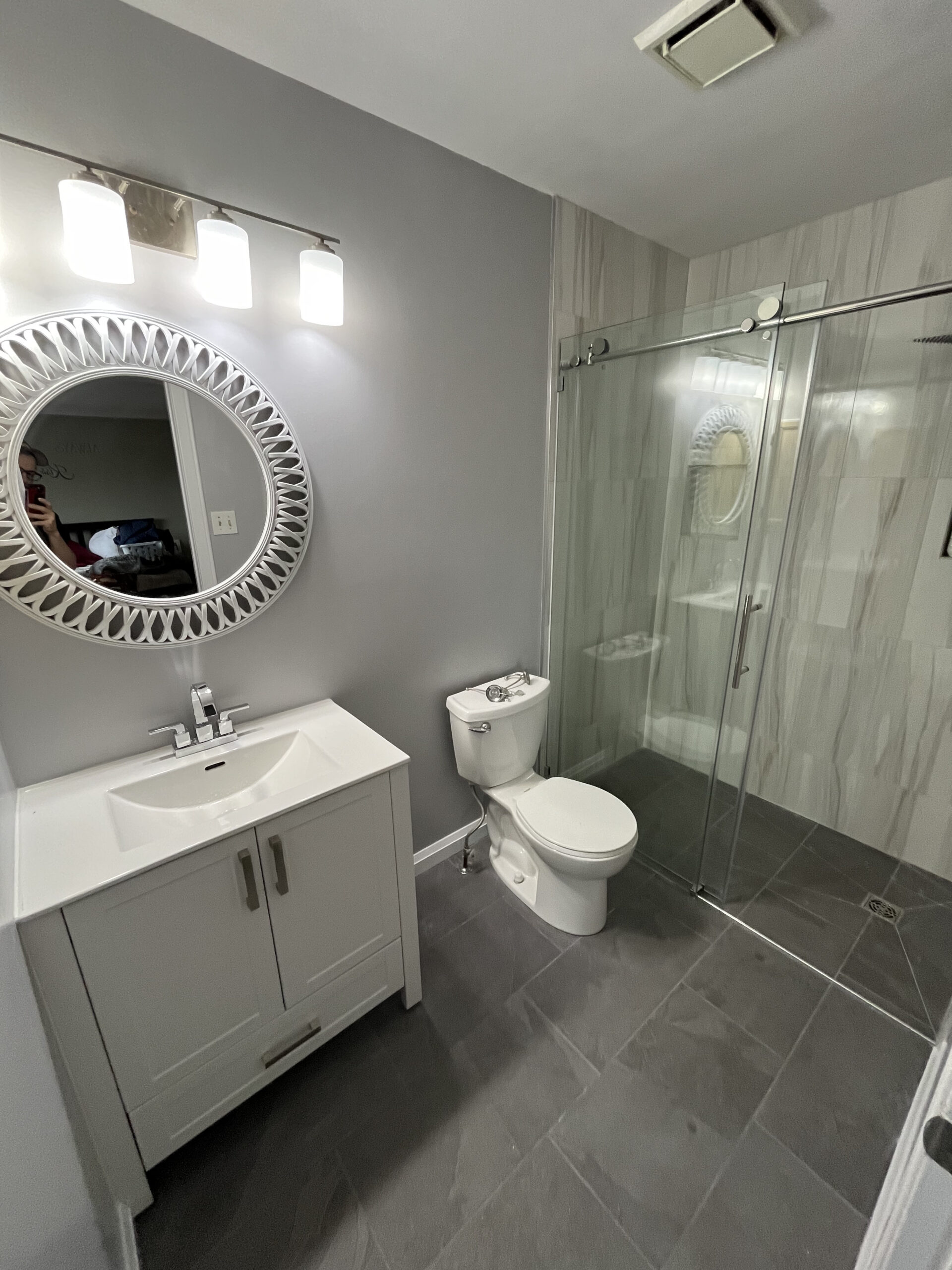 Beautiful modern bathroom with dark slate gris tiles, a seamless shower with glass sliding door and a white vanity